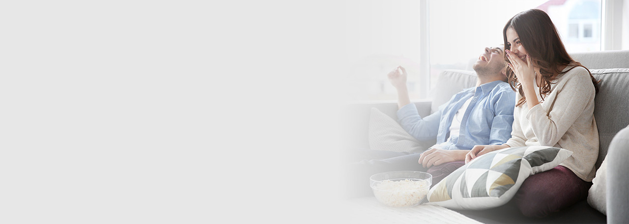 Pariskunta istumassa nauraen sohvalla syömässä popcornia.