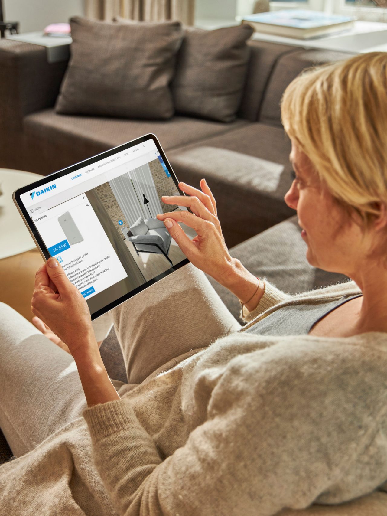 Nainen istuu sohvalla katsellen ilmastointilaitteita virtuaalikokemuskeskuksessa tabletillaan